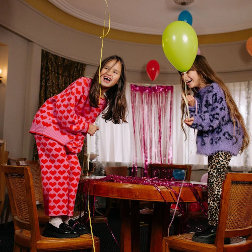 Two children playing with balloons in a room with a table and chairs.