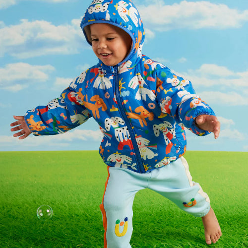 Child wearing a colorful raincoat with animal patterns on a grassy field with a blue sky.