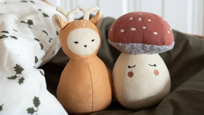 Two soft toys, one resembling a deer and the other a mushroom, on a textured surface.