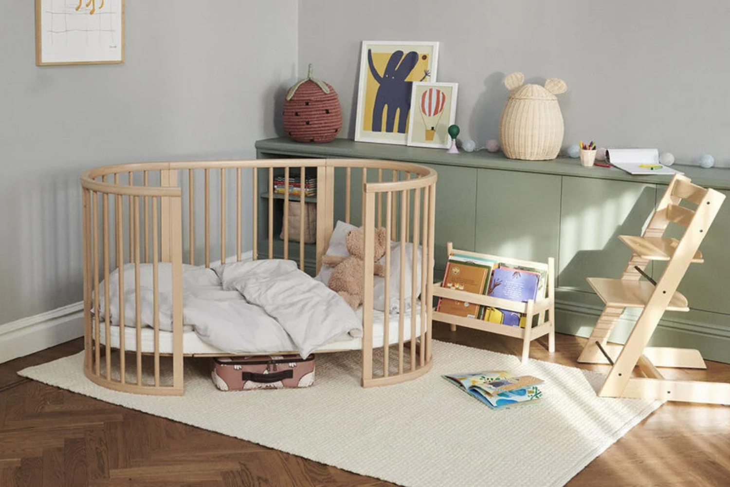 Wooden Stokke crib in a child's room with toys and furniture.
